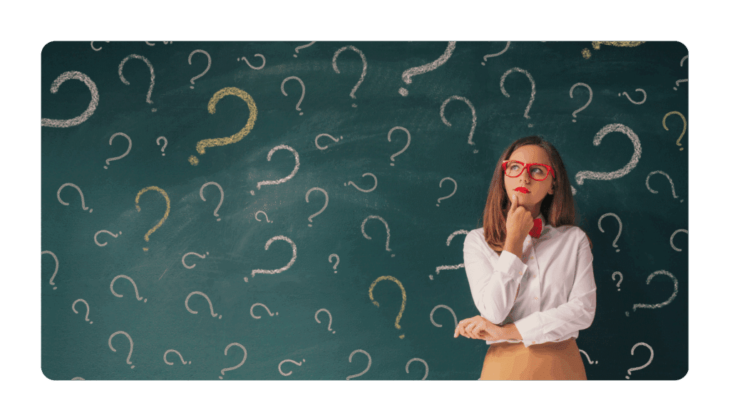 woman standing at a blackboard that is covered in question marks looking curious